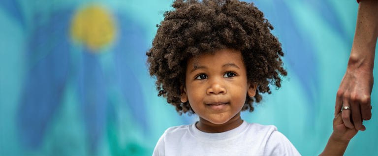 A close-up of a child in front of a mural with dark blue and yellow flowers.
