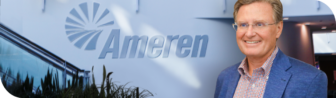 A man in a blue blazer and checkered shirt smiles in front of a wall with the Ameren logo. The background includes plants and a staircase with metal railings.