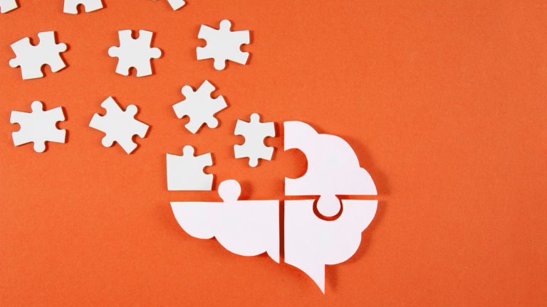 white puzzle pieces on an orange background, making up a white image of a brain