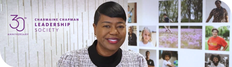 United Way President and CEO poses infront of gallery of photos. The words "30th Anniversary Charmaine Chapman Leadership Society" are written on the left hand side